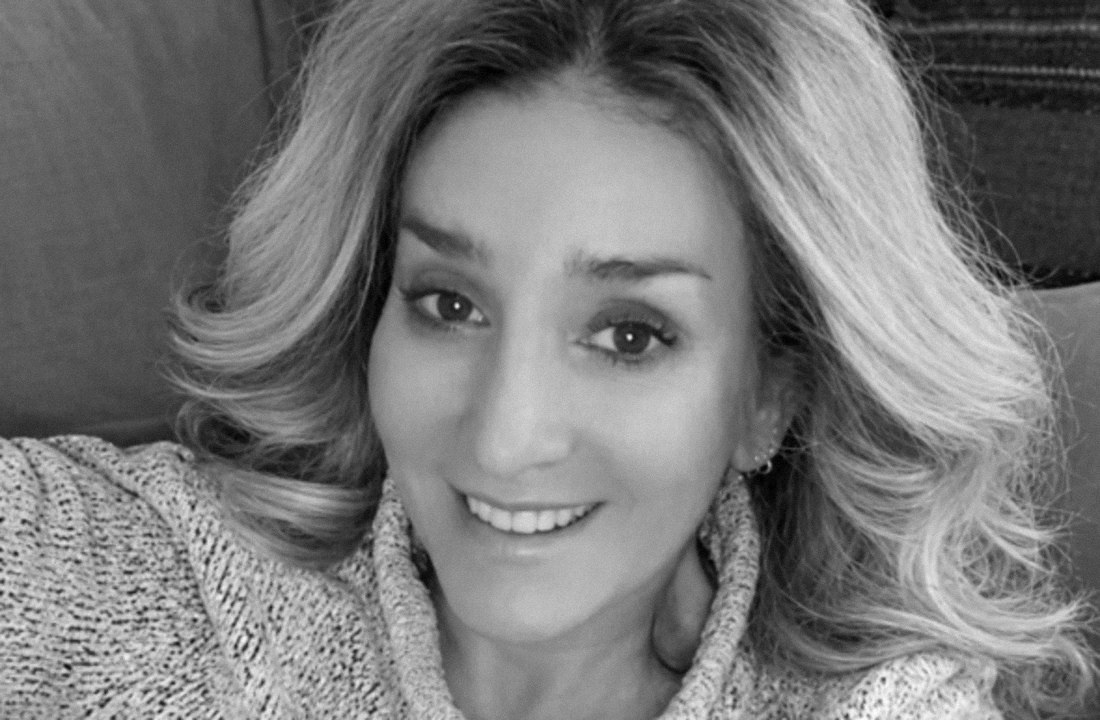 Black-and-white photograph of Stevie smiling on the sofa in a grey knit jumper